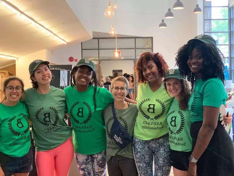 7 young women in green Barnard Sustainability shirts with their arms around each other